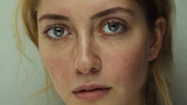 Close-up portrait of a woman with grey eyes and visible skin texture.
