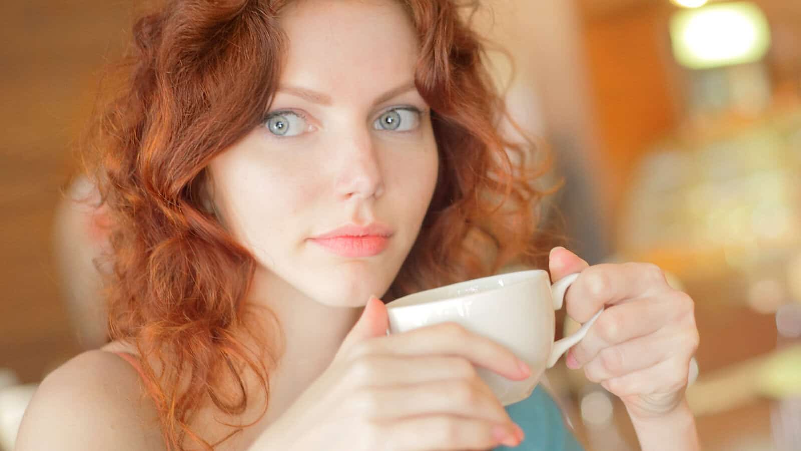 A young woman with red hair holding a white coffee cup.