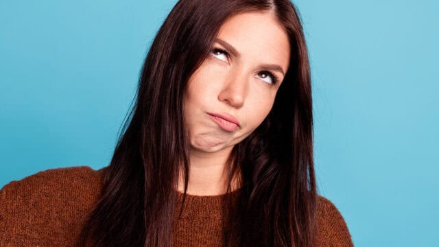 A young woman with long dark hair looking upward with an annoyed expression.