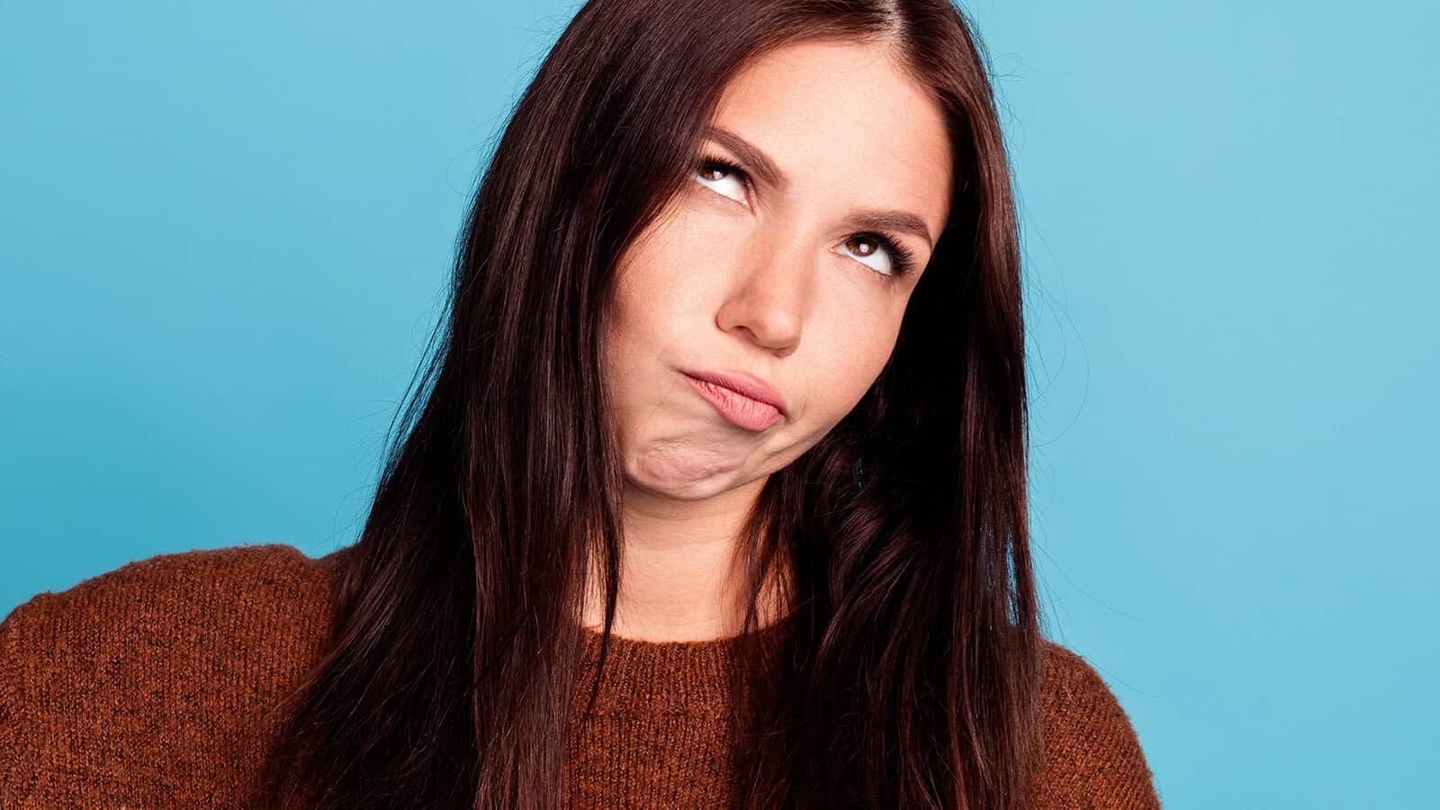 A young woman with long dark hair looking upward with an annoyed expression.