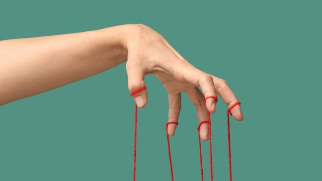 A human hand with red strings tied around four fingers, held as if controlling a marionette.