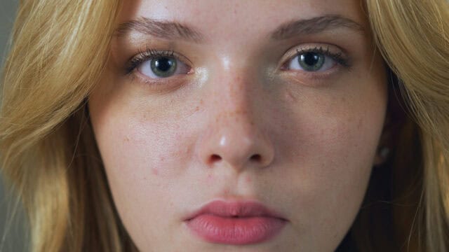Close-up portrait of a woman with blonde hair and green eyes looking directly at the camera.