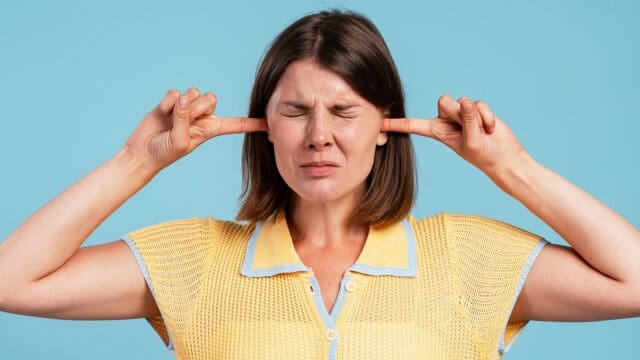 A woman with her eyes tightly closed presses her index fingers into her ears.