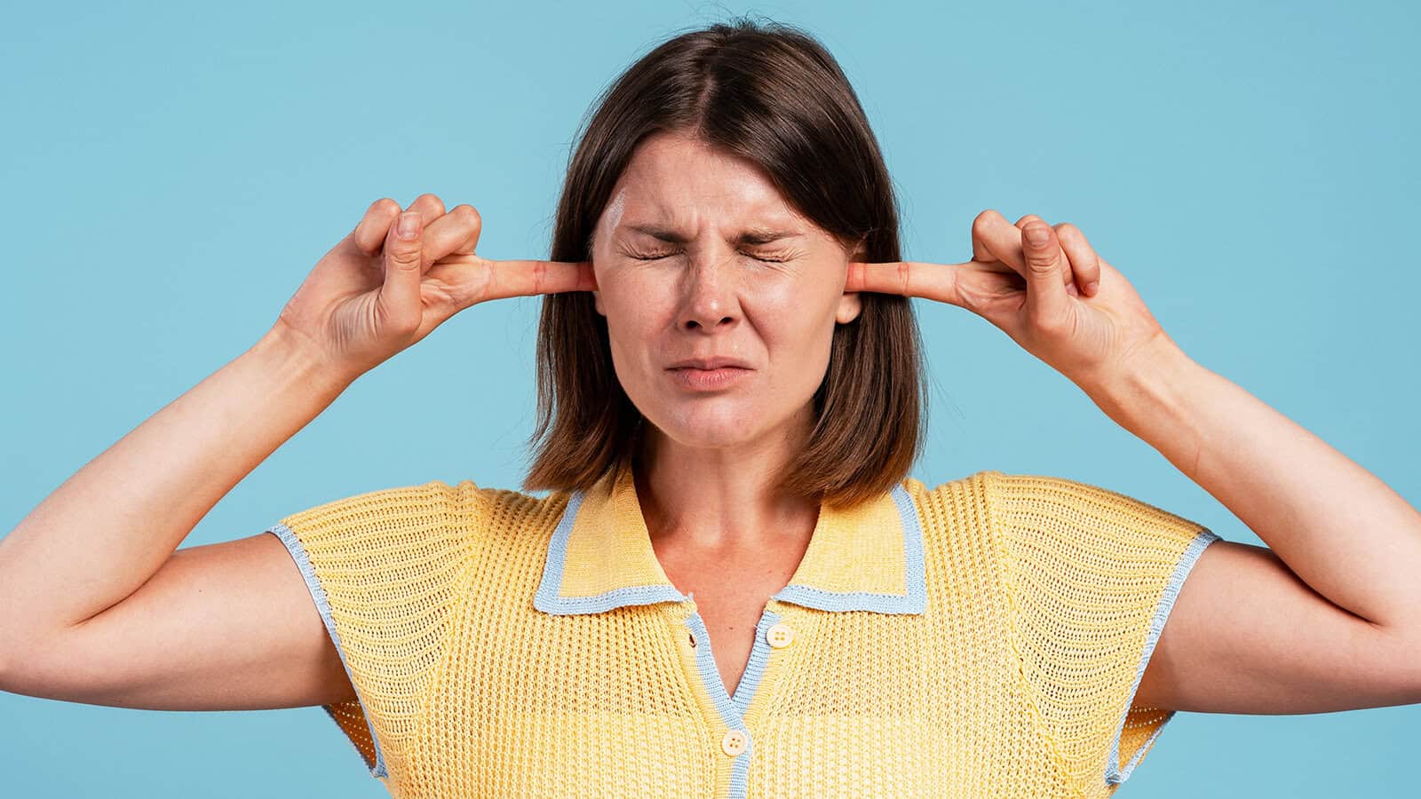 A woman with her eyes tightly closed presses her index fingers into her ears.