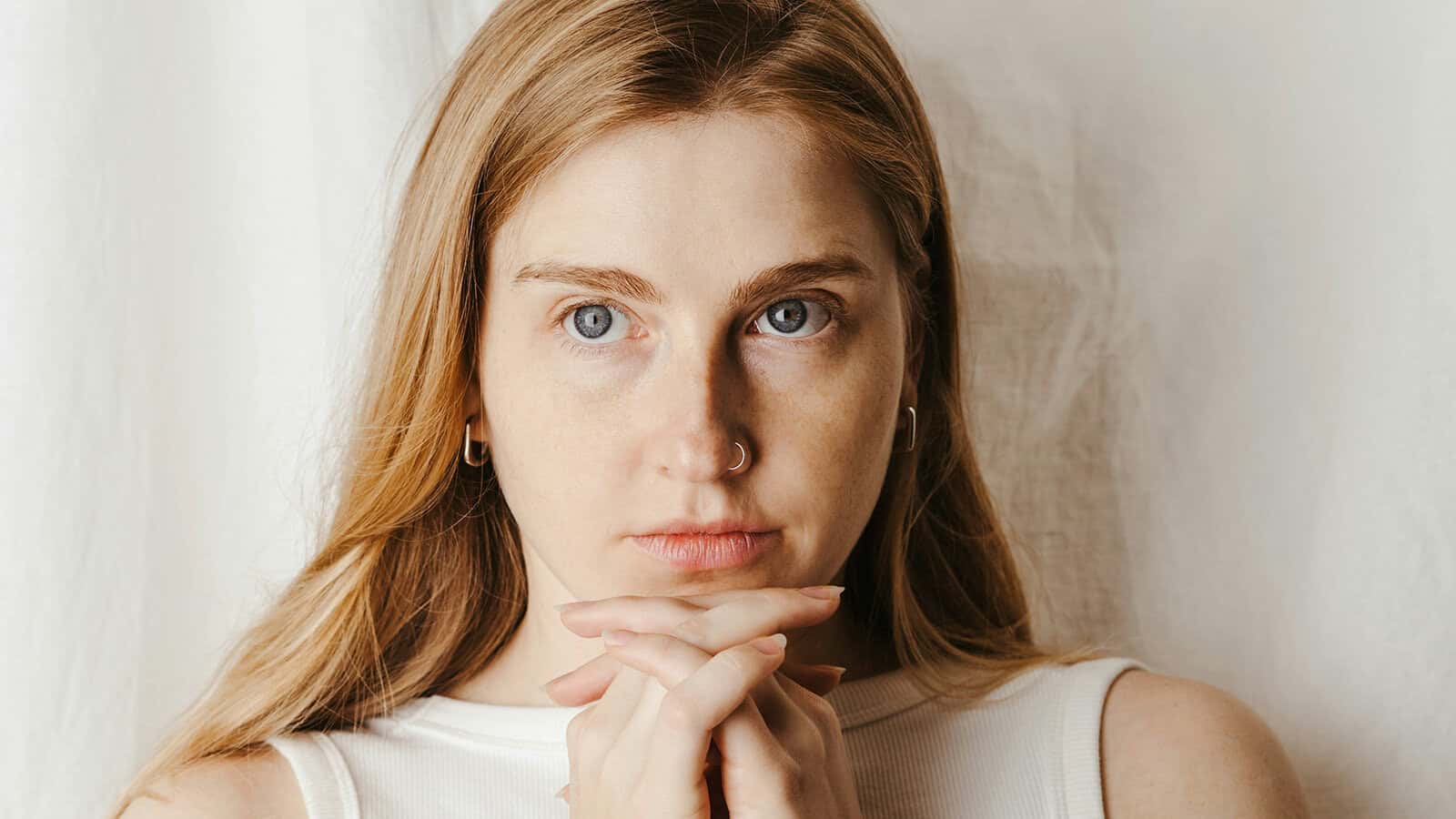 Close-up portrait of a woman with her hands clasped under her chin, looking directly at the camera.