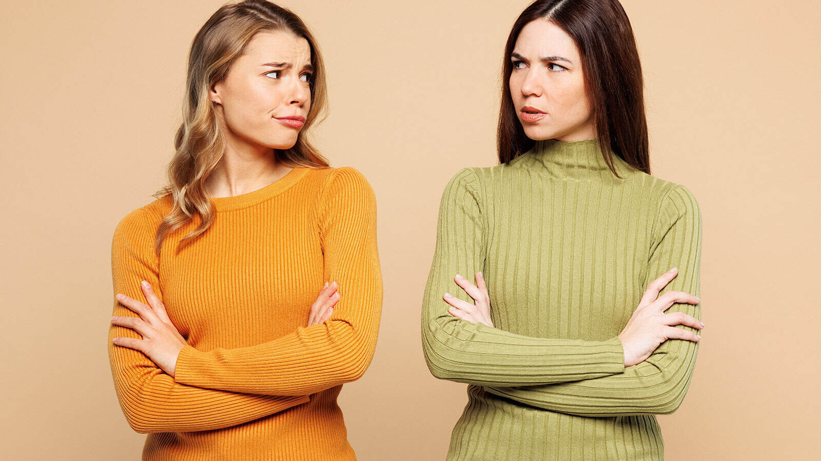 Two women standing with their arms crossed, looking at each other with skeptical expressions.