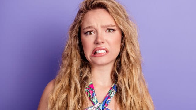 A young woman with long blonde hair looks at the camera with a grimacing, skeptical expression.