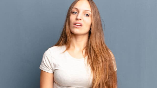 A young woman with long hair looking toward the camera with a skeptical or confused expression.