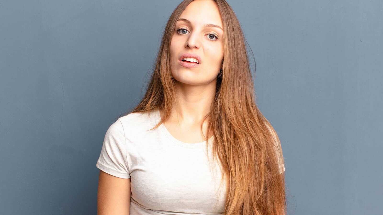 A young woman with long hair looking toward the camera with a skeptical or confused expression.