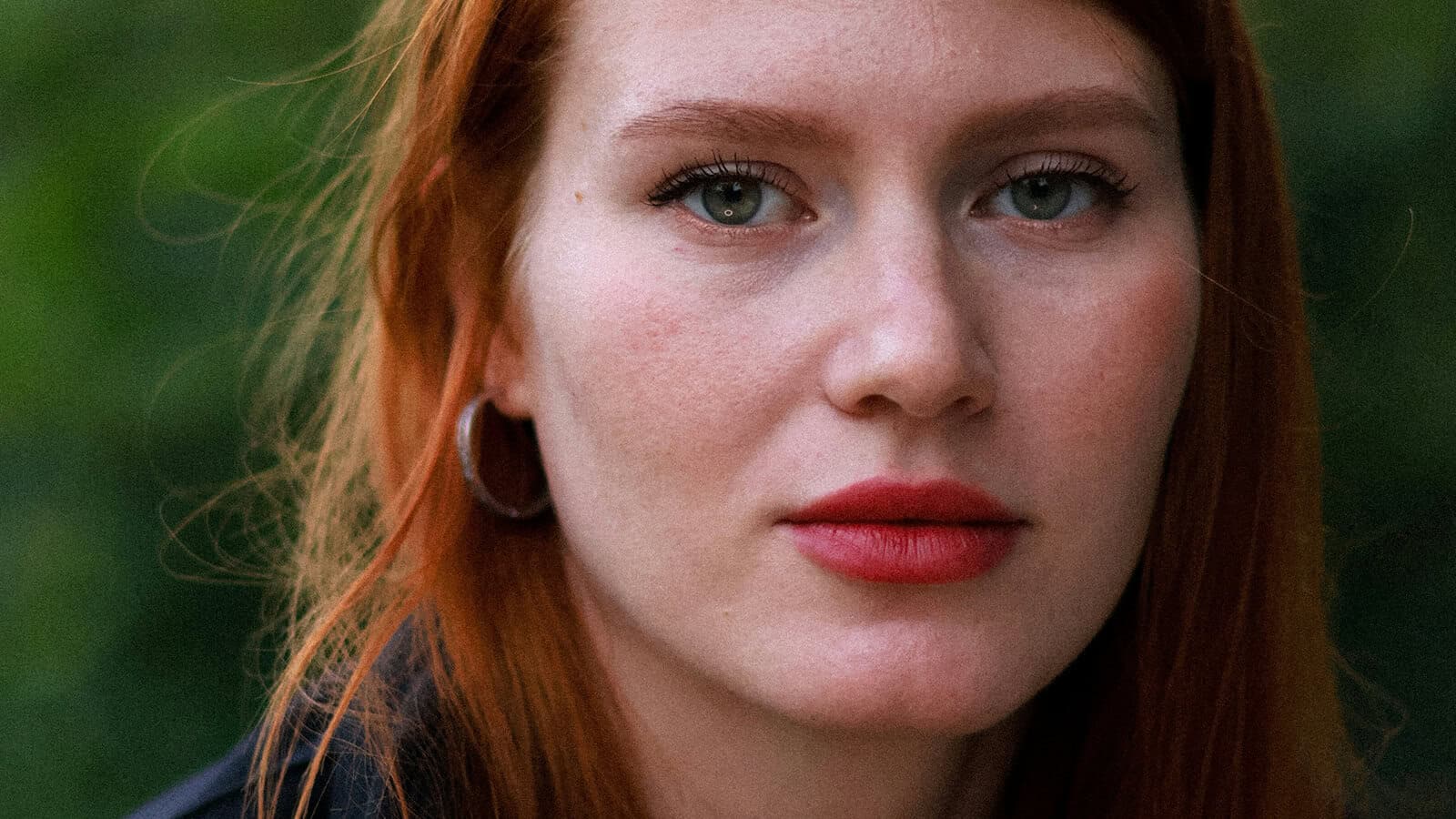 Close-up portrait of a woman with red hair and red lipstick looking directly at the camera.