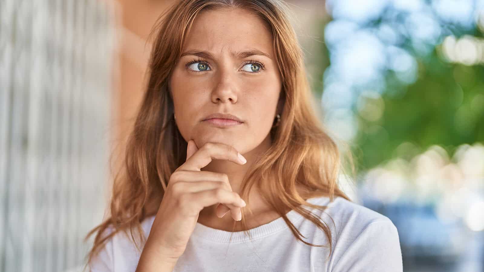 A young woman looking thoughtful with her hand on her chin.