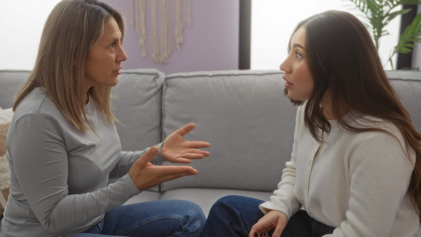 Two women sit on a sofa facing each other, engaged in a conversation.