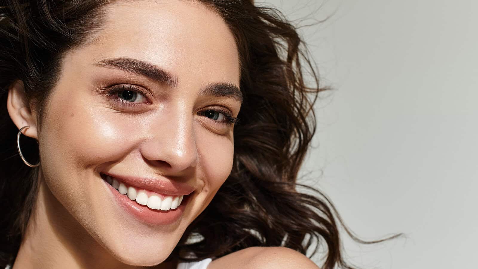 A close-up portrait of a smiling woman with wavy hair and hoop earrings.