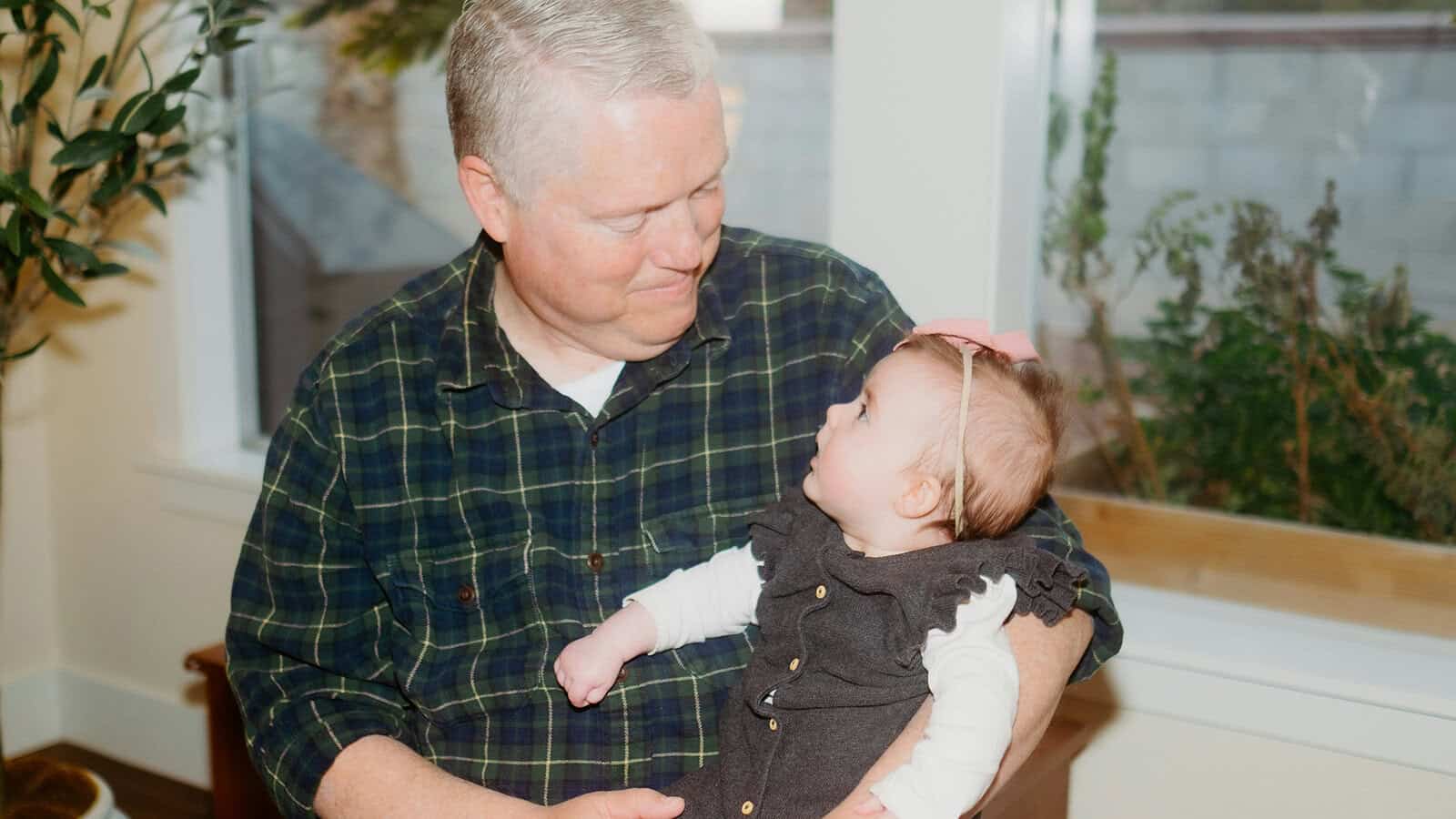 A man in a plaid shirt holds a baby, looking at each other affectionately.