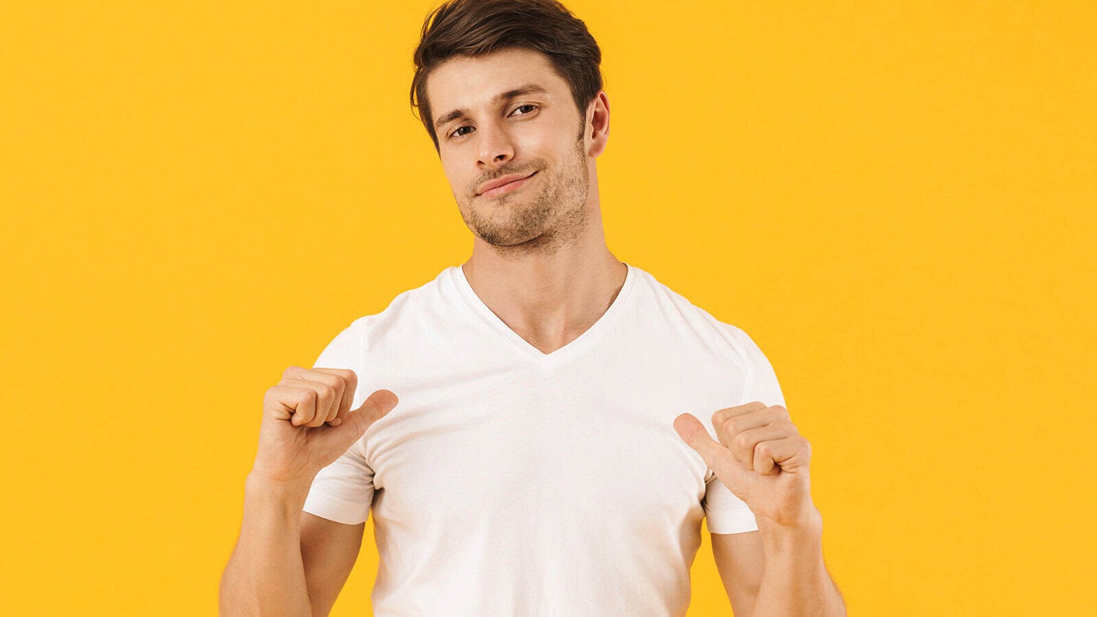 A man in a white t-shirt points both thumbs toward himself and smiles slightly, standing against a bright yellow background.