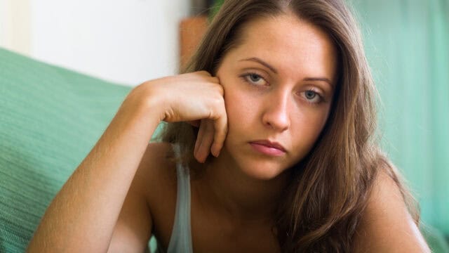 A woman rests her chin in her hand with a pensive expression.