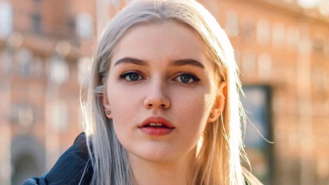 Close-up portrait of a young woman with platinum blonde hair looking directly at the camera.