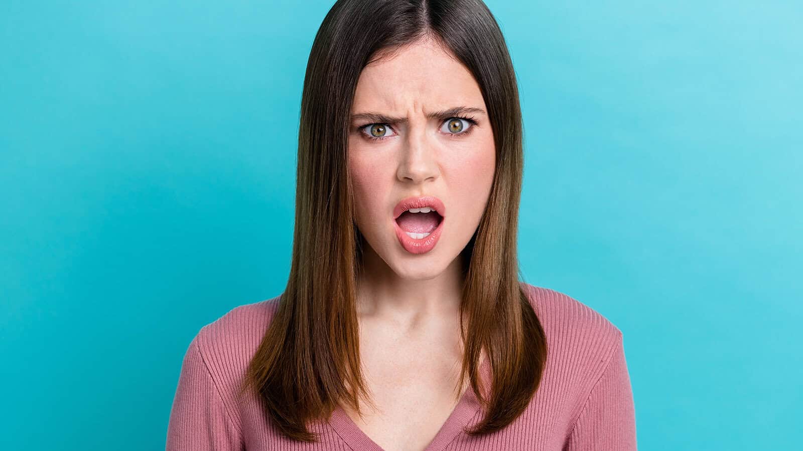 A young woman with a shocked expression, her mouth slightly open, against a turquoise background.
