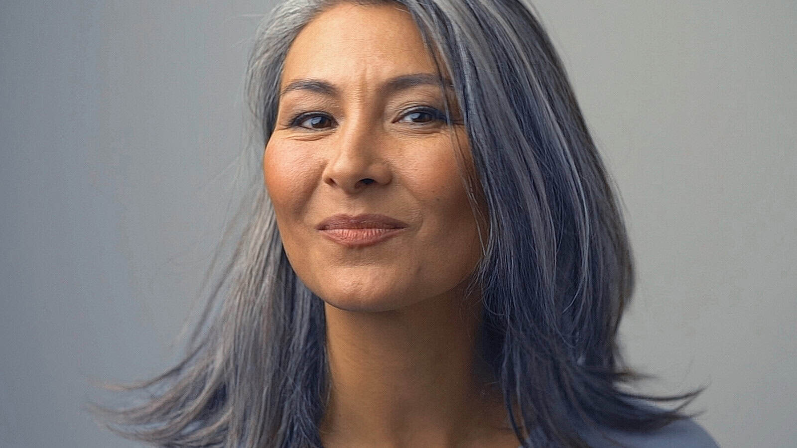 Close-up portrait of a smiling woman with long grey hair.