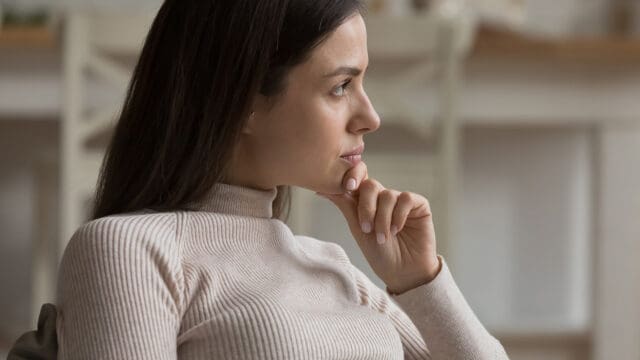 A woman rests her chin on her hand, looking thoughtfully to the side.
