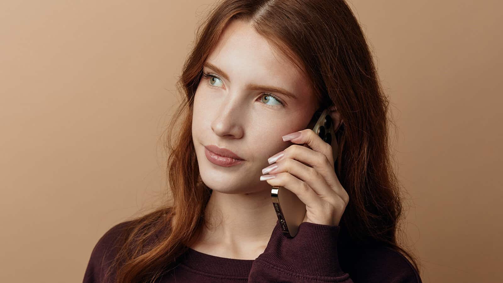 A woman with long red hair holds a smartphone to her ear.