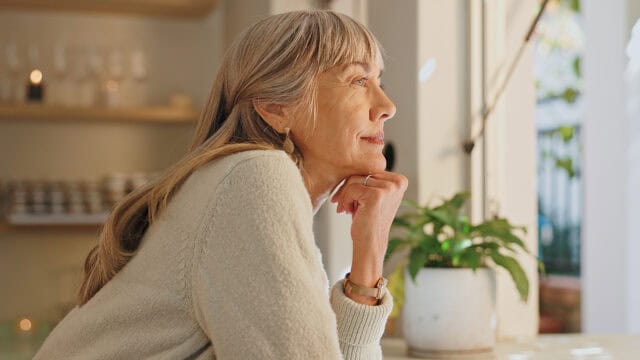 A woman with long blonde hair resting her chin on her hand, looking out a window.