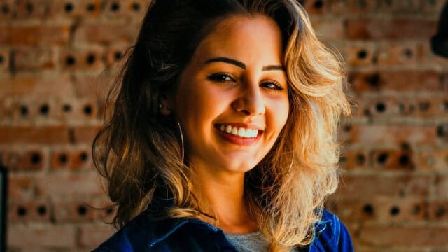 A smiling woman looking at the camera in front of a brick wall.