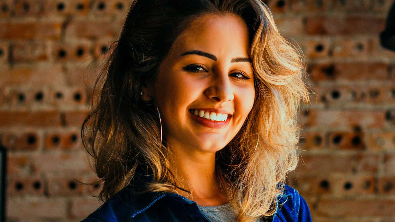 A smiling woman looking at the camera in front of a brick wall.