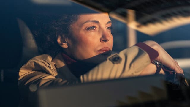 A woman sitting in the drivers seat of a car, looking out the window.