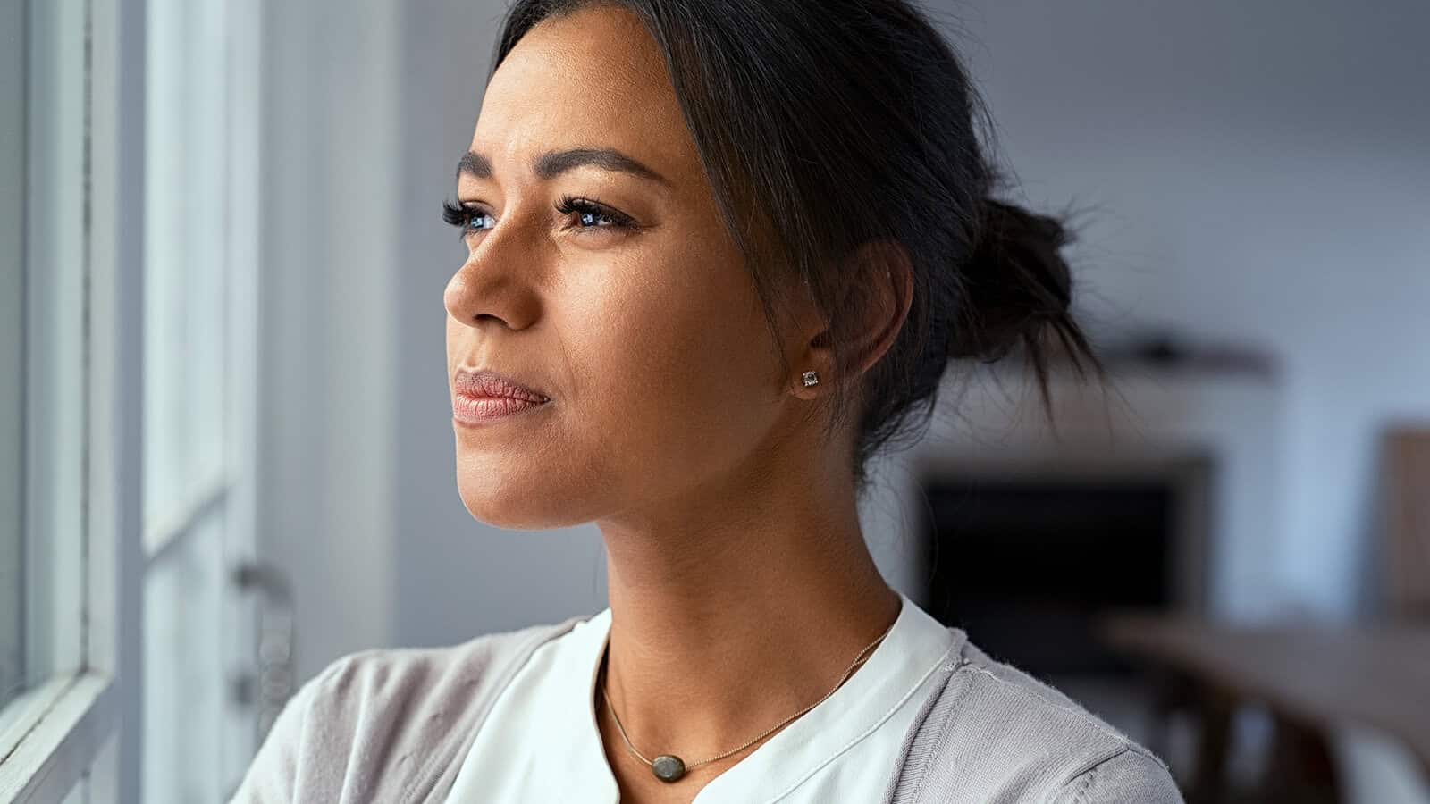 A woman looking out a window with a thoughtful expression.