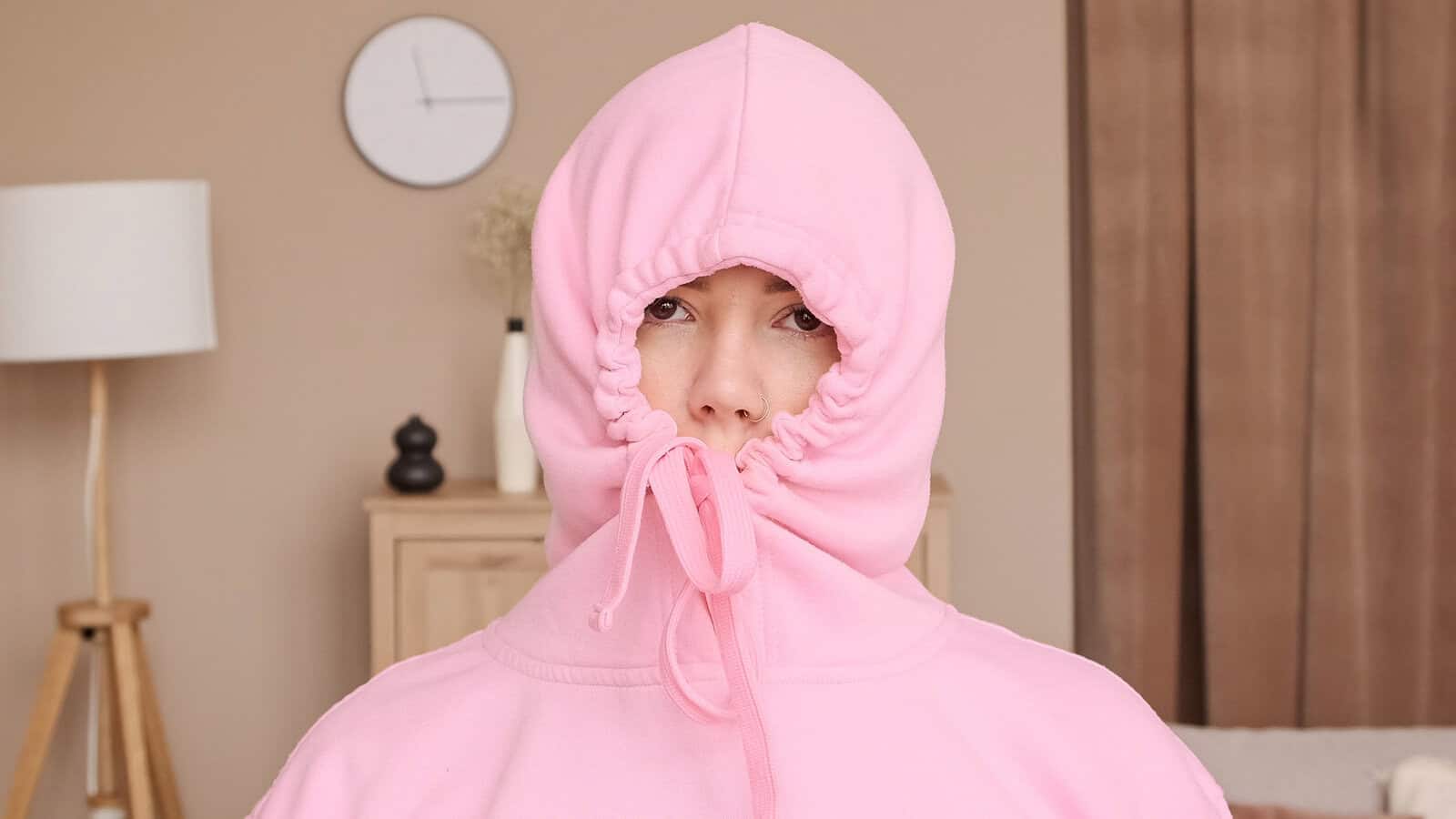 A person wearing a pink hooded sweatshirt with the drawstring pulled tight around their face.