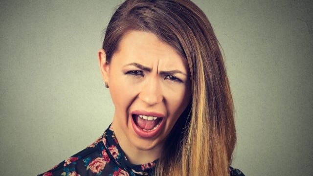 A young woman with a frustrated and annoyed expression looking directly at the camera with her mouth open.