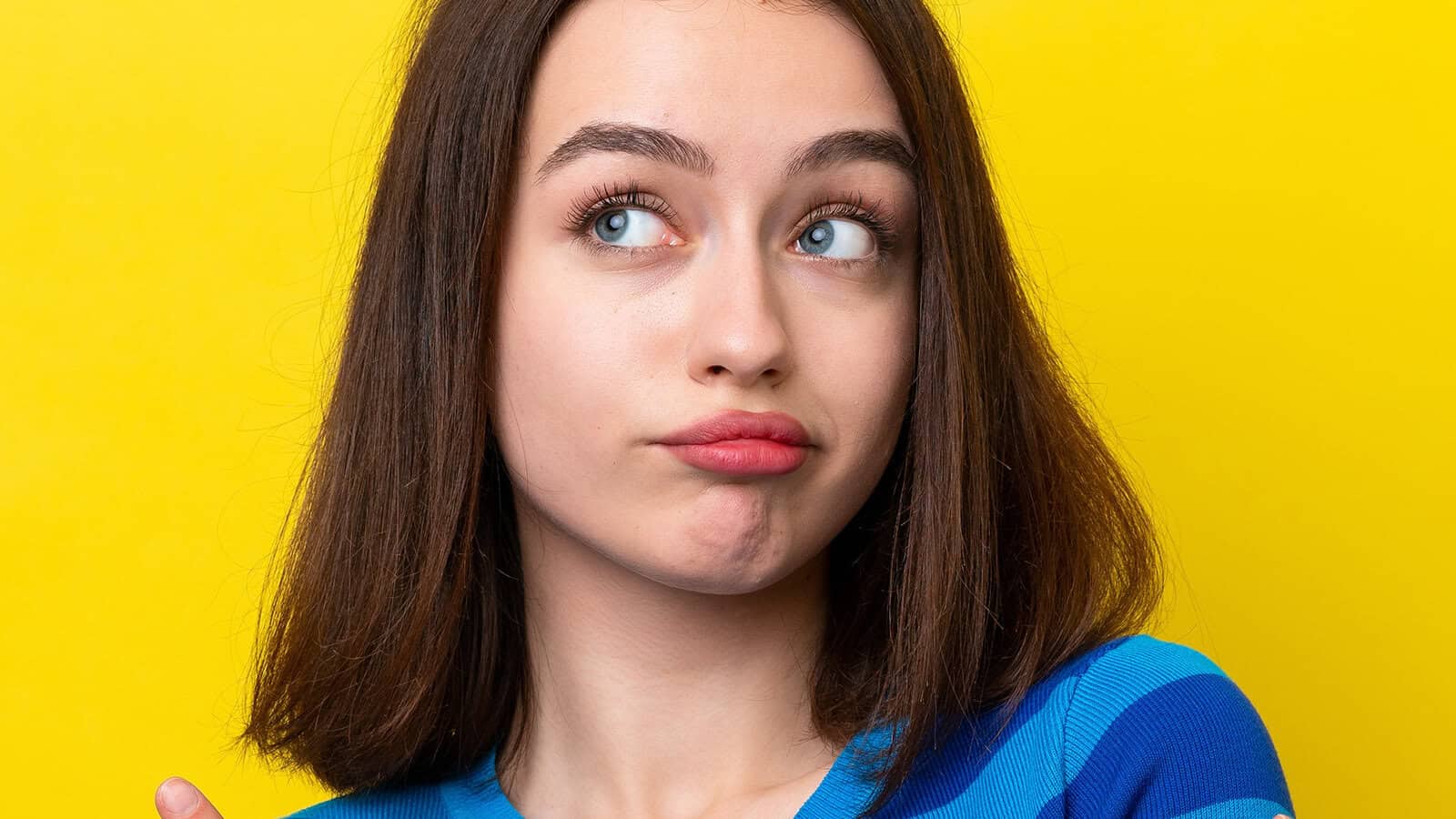 A young woman with brown hair looks upward with a thoughtful, skeptical expression against a bright yellow background.