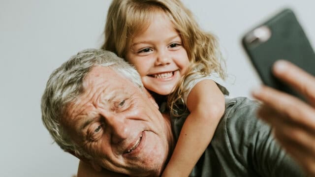 A young girl smiling as she takes a selfie with her grandfather.