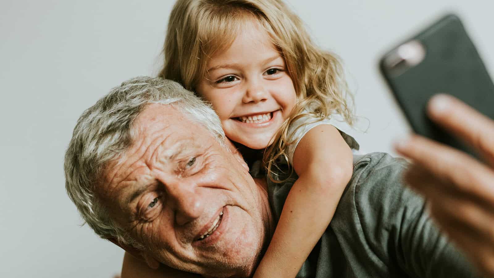 A young girl smiling as she takes a selfie with her grandfather.