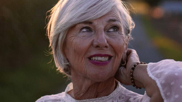 Close-up of a smiling older woman with short gray hair, looking upward.
