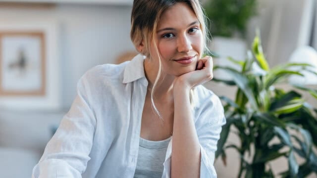 A woman in a white shirt resting her chin on her hand, smiling at the camera.