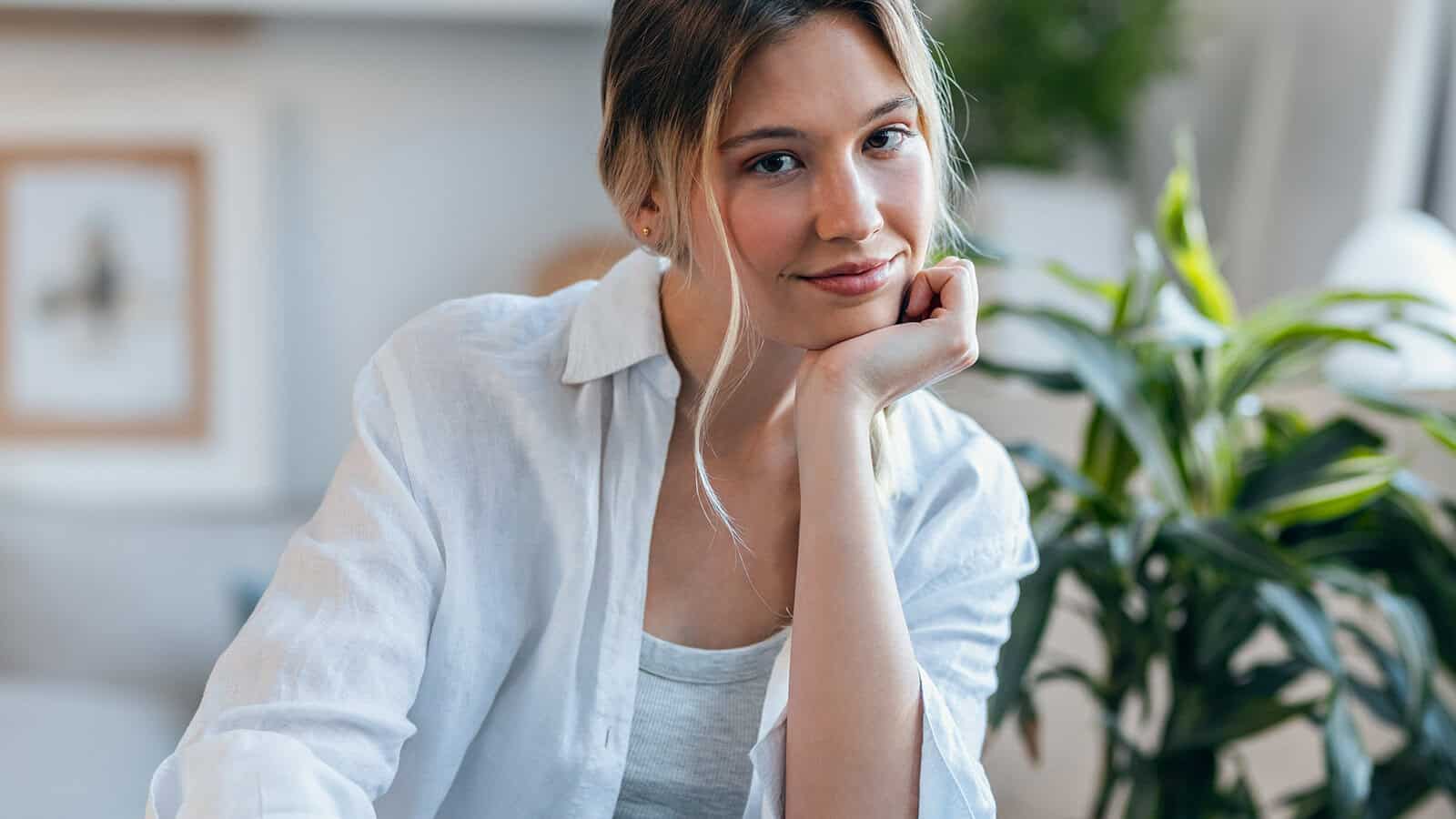 A woman in a white shirt resting her chin on her hand, smiling at the camera.