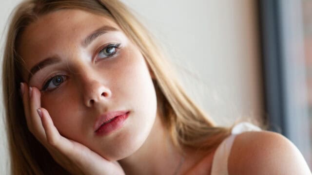 A close-up portrait of a young woman resting her chin on her hand and looking thoughtfully to the side.