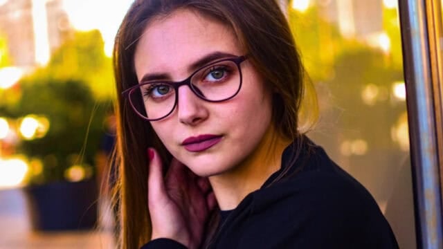 A young woman with dark-rimmed glasses looking directly at the camera.