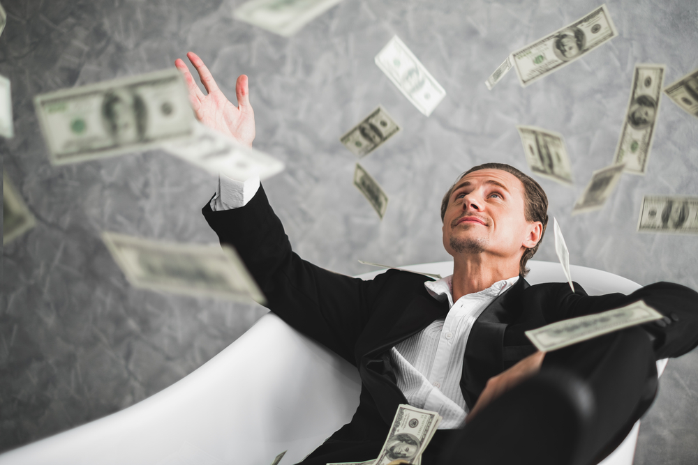 A rich and happy middle aged man in a bathtub and spraying money into the air
