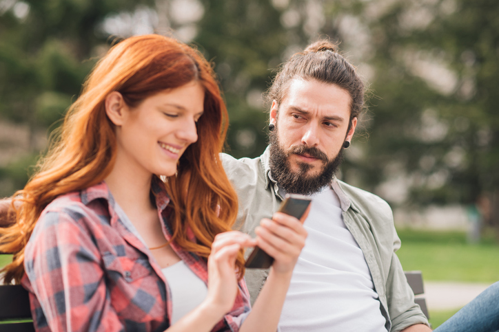 Angry man looking at happy woman text messaging