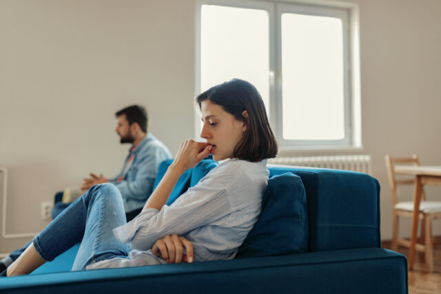 Unhappy Couple After an Argument in the Living Room at Home. Sad Pensive Young Girl Thinking of Relationships Problems Sitting on Sofa With Offended Boyfriend, Conflicts in Marriage, Upset Couple After Fight Dispute, Making Decision of Breaking Up Get Divorced