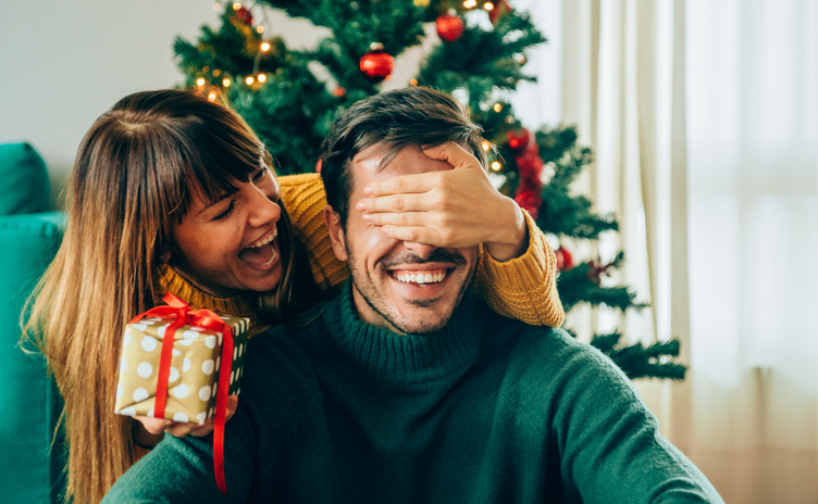 Young woman standing behind her boyfriend with a gift.