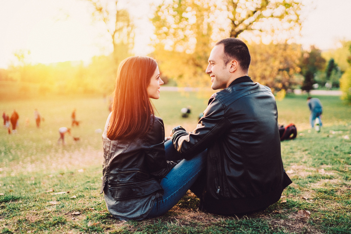 A couple starring into each other's eyes while sitting on the bare ground in a park and holding hands