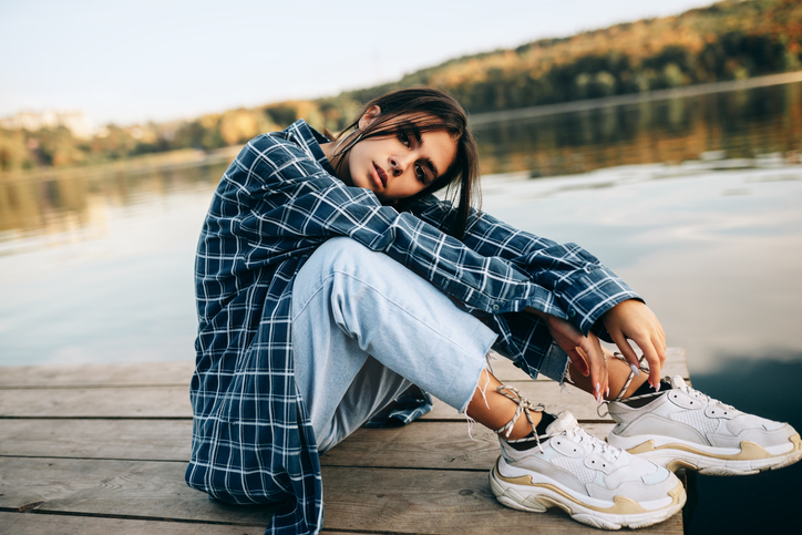 Young woman sitting on a dock near a lake or river looking sad / disassociated/ lonely