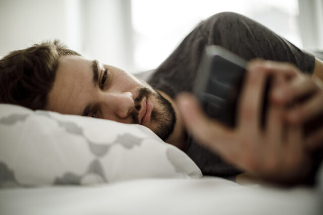 Man in bed text messaging.