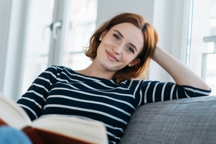 Pretty young woman relaxing on a sofa at home reading a book