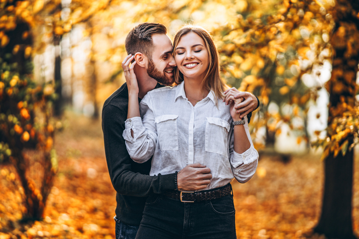 A young couple in love walking in the autumn park on a sunny day. The man gently hugs the woman. Love story.
