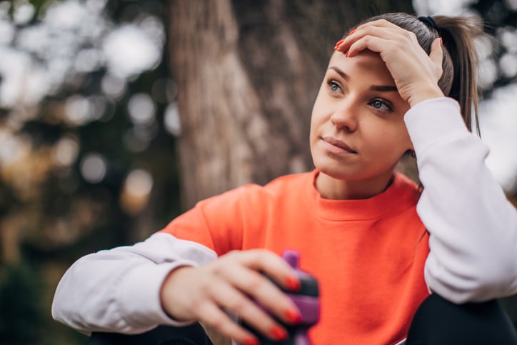 One young attractive fitness woman taking a break after jogging in public park.